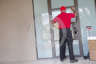 Rear view of a delivery man with packages knocking at door