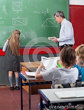 Rear View Of Little Schoolgirl Writing On Board