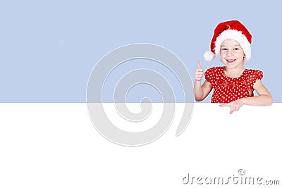 In a red dress and hat of Santa Claus a little girl shows a finger on a billboard