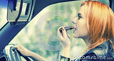 Red haired woman applying lipstick on lips in car. Danger on road.
