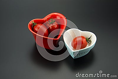 A red heart-shaped bowls and a blue heart-shaped bowls, and red tomatoes