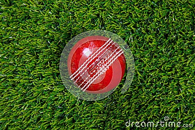 Red leather cricket ball on grass
