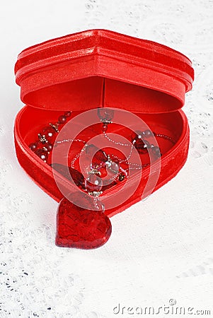 Red necklace in heart jewelry box on a white lace tablecloth.