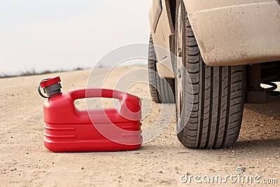 Red plastic fuel canister on dirt road with car