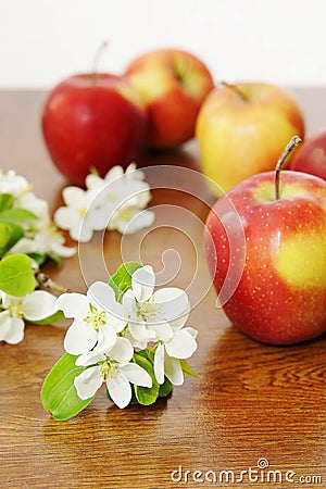 Red ripe apple fruits and white apple flowers on a wooden tabl