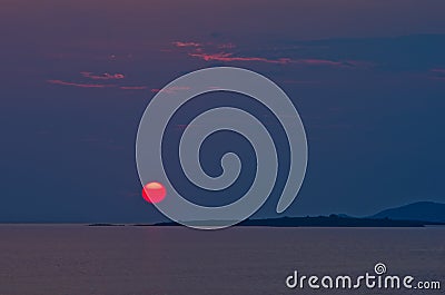 Red sun and sunset at sea below small cape at Sithonia