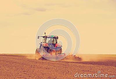 Red tractor driven by farmer cultivating land at spring.