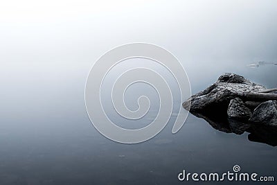 Reflections of rocks in a foggy lake