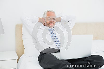 Relaxed businessman looking at laptop in bed