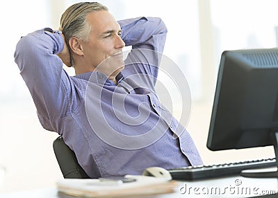 Relaxed Businessman Sitting With Hands Behind Head At Desk