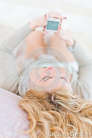 Relaxed woman at home reading a text message in her bright bedro