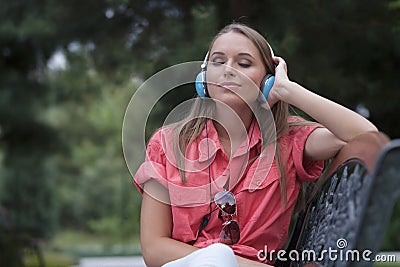 Relaxed young woman listening to headphones on park bench