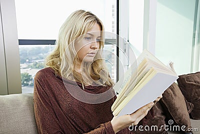 Relaxed young woman reading book in living room at home