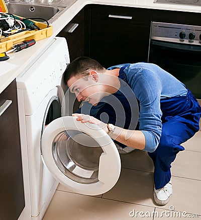 Repairman in uniform repairing washing machine