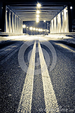 Road by illuminated bridge at night