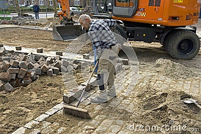 Road worker sweeps sand between cobblestones