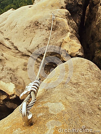 Rope end anchored for climbers into sandstone rock. Iron twisted rope fixed with srew clamps in block. Safety footpath between roc