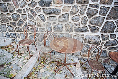 Round table and some chairs standing at stone wall of cafe