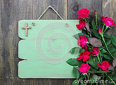 Rustic green blank sign with wooden cross and flower border of red roses hanging on wood door