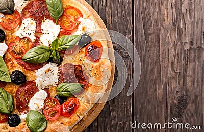 Rustic pizza with salami, mozzarella, olives and basil on wooden