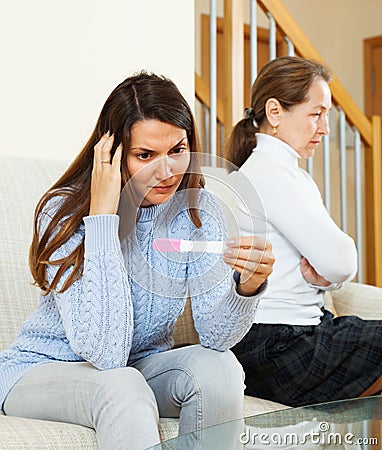 Sad girl with pregnancy test against mature mother