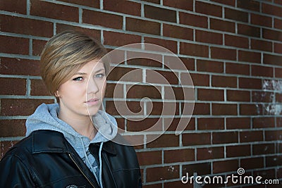 Sad girl sitting outside brick wall in school yar