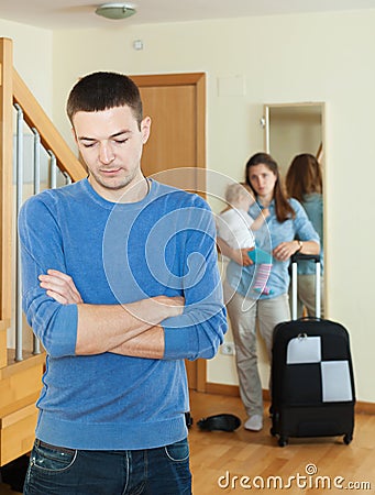 Sad man against wife with baby and suitcase