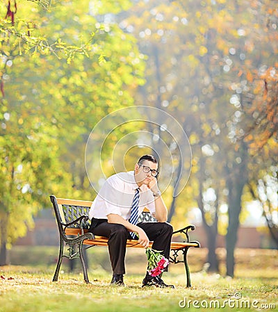 Sad young man holding flowers and sitting on a bench in a park