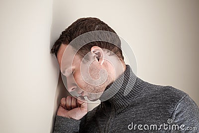 Sad young man rested his head and fist on wall