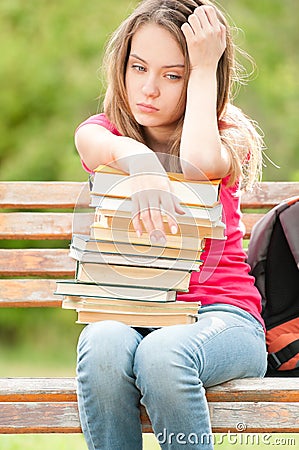 Sad young student girl sitting on bench with books