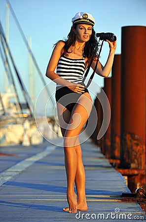 Sailor model in stylish swimsuit holding binoculars and standing on the wooden pier