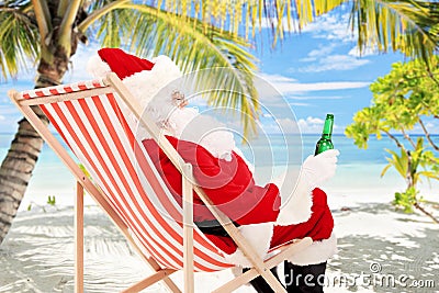 Santa Claus on a chair drinking beer and enjoying on a beach