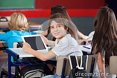 Schoolboy With Digital Tablet Sitting At Desk In