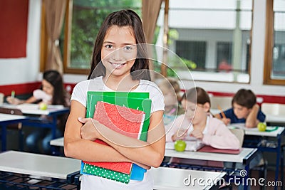 Schoolgirl Holding Books While Standing At Desk