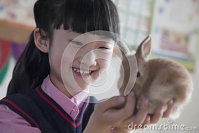 Schoolgirl holding pet rabbit in classroom