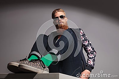 Seated bearded young man looks down at you