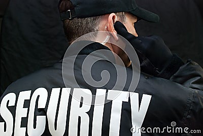 Security Guard Listens To Earpiece, Back of Jacket Showing