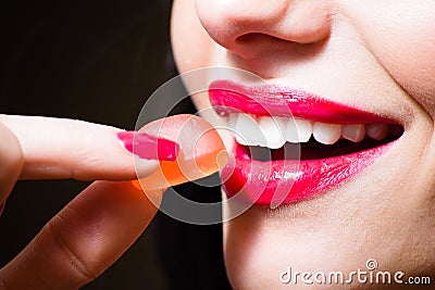 Seductive charming beautiful red lips and red color nails hand holding candy at white healthy teeth closeup
