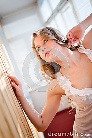Seductive young pretty woman in pajamas looking up on balcony with shutters light on background portrait
