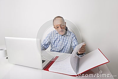 Senior businessman using laptop while reading file at office desk