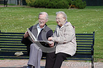 Senior couple reading newspaper on a park bench