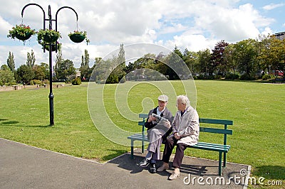 Senior couple reading a newspaper on a park bench