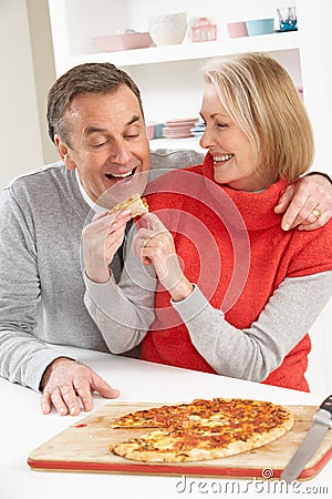 Senior Couple Sharing Takeaway Pizza In Kitchen