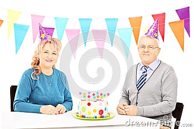 Senior couple sitting on table with big cake and celebrating bir