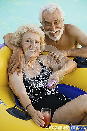 Senior Couple in Swimming Pool woman lying on inflatable raft holding drink listening to portable music player portrait.