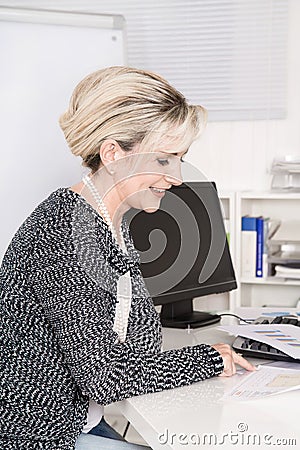 Senior female worker sitting at desk looking at business paper.