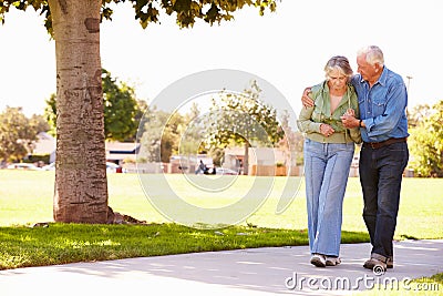 Senior Man Helping Wife As They Walk In Park Together