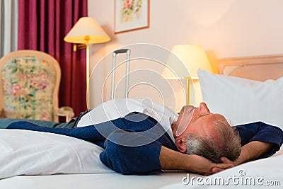 Senior man lying on the bed in the hotel room