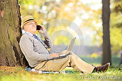 Senior man in park talking on a phone and working on laptop