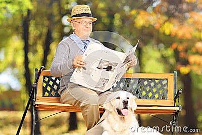 Senior man seated on a bench reading a newspaper with his dog